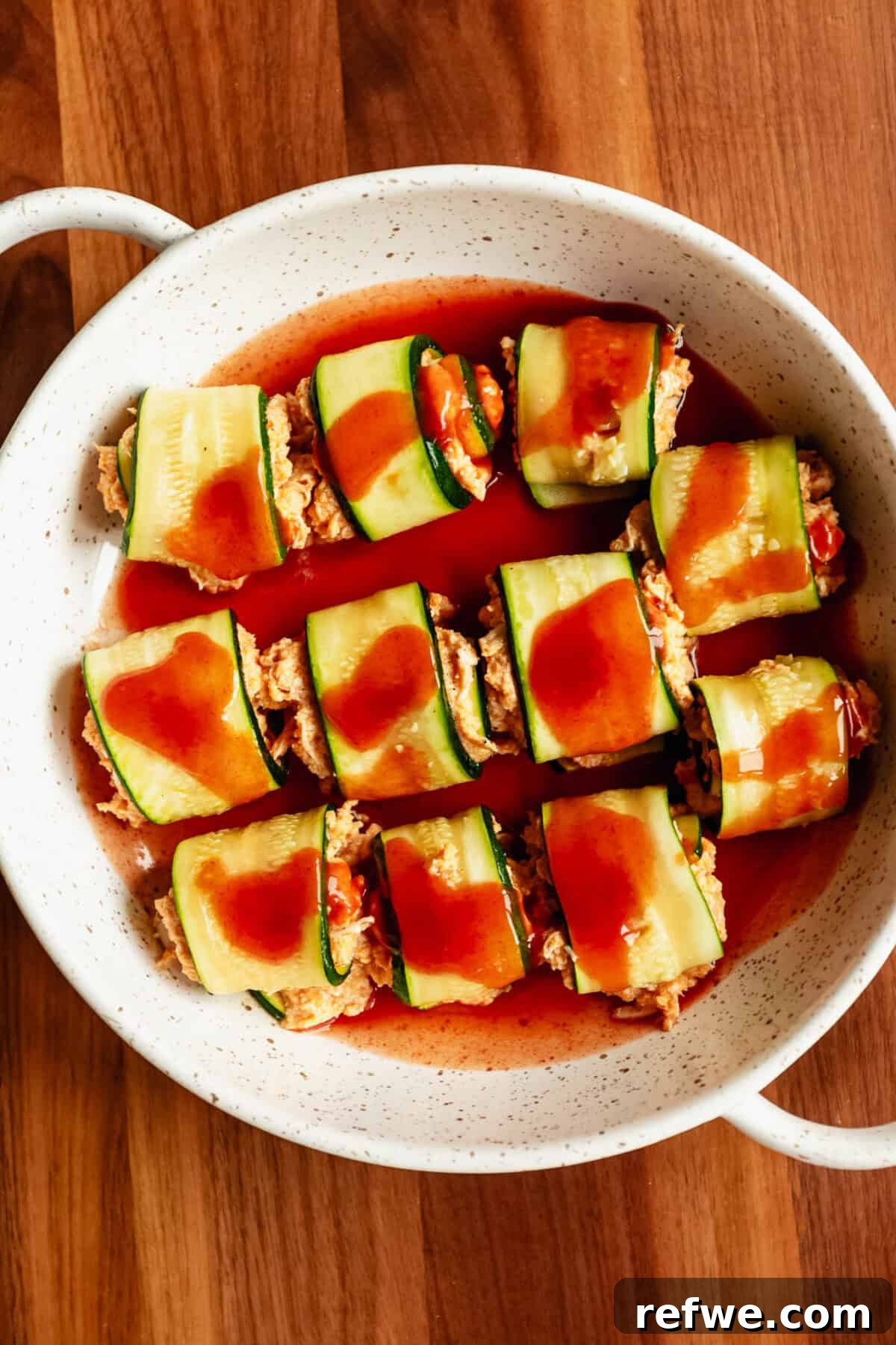 Buffalo Chicken Zucchini Roll-Ups Recipe 10 buffalo chicken zucchini roll ups in a baking dish with hot sauce.