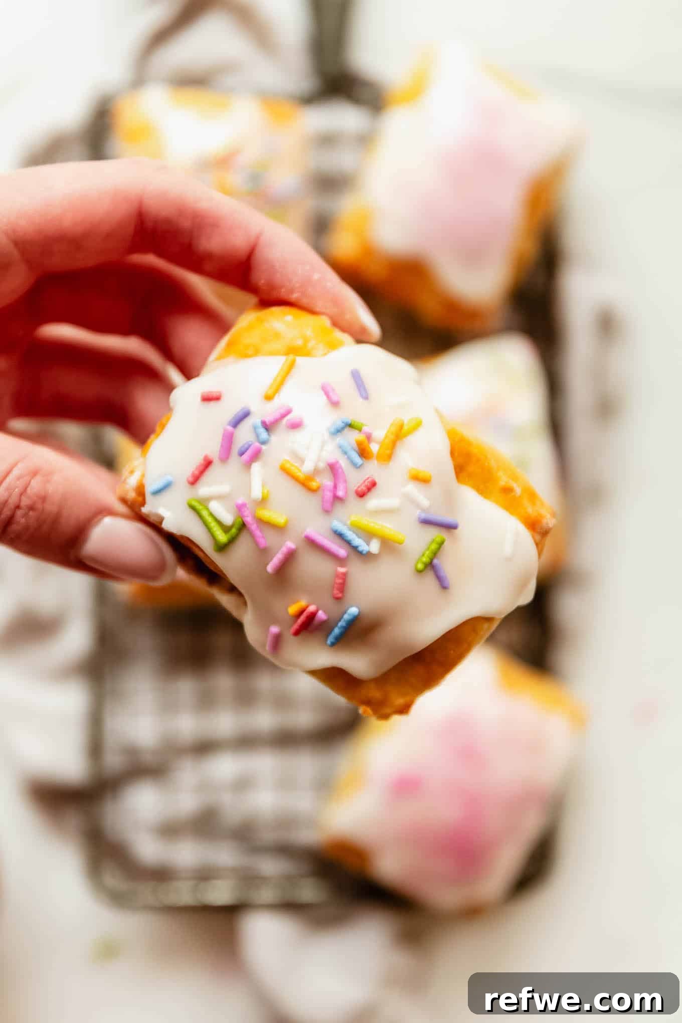 Homemade Cottage Cheese Pop Tarts Recipe 13 a hand holding a Cottage cheese dough pop tart topped with icing and rainbow sprinkles.