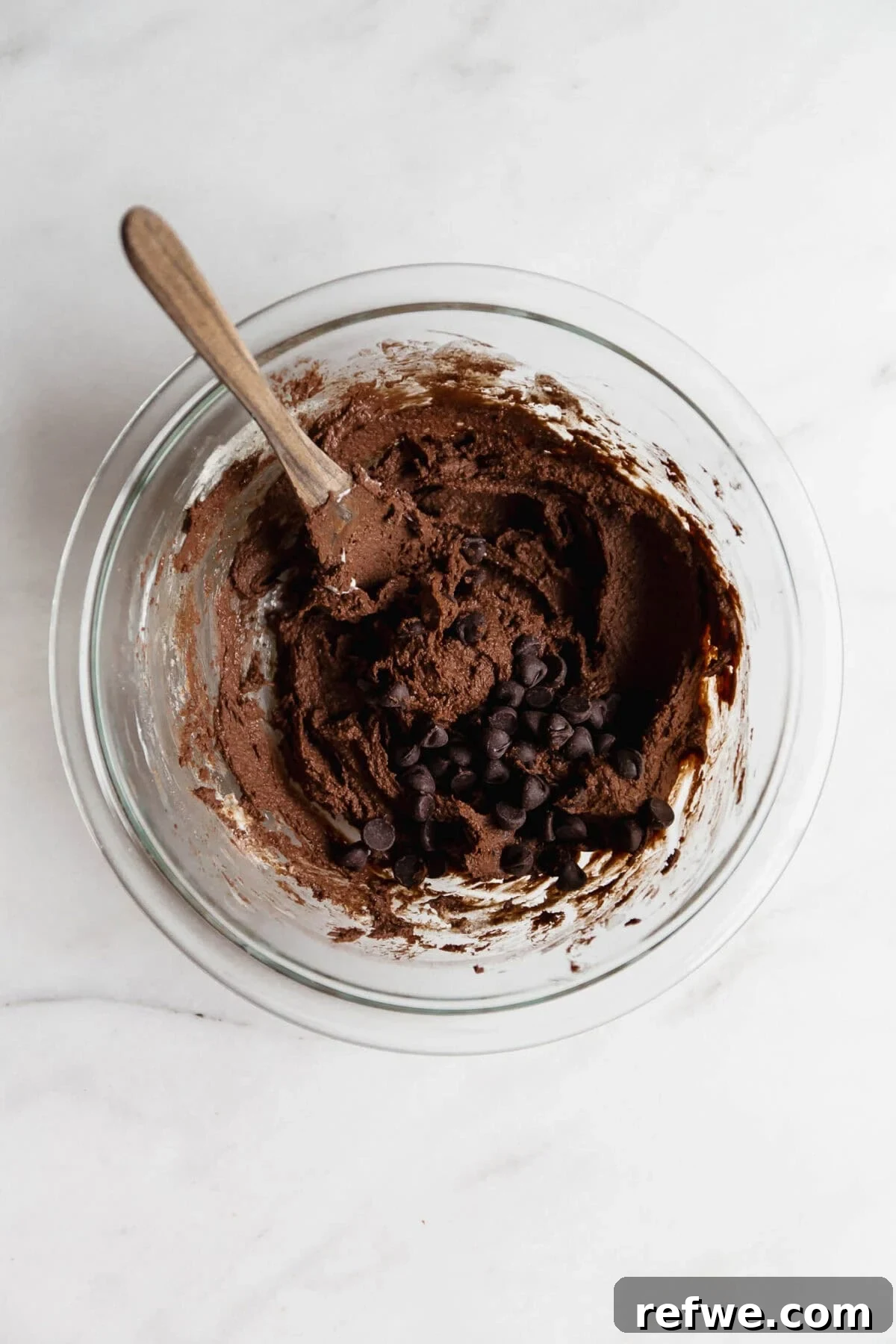 Cottage Cheese Brownie Batter Recipe 8 Cottage cheese brownie batter in a clear mixing bowl with a wood spoon and chocolate chips.