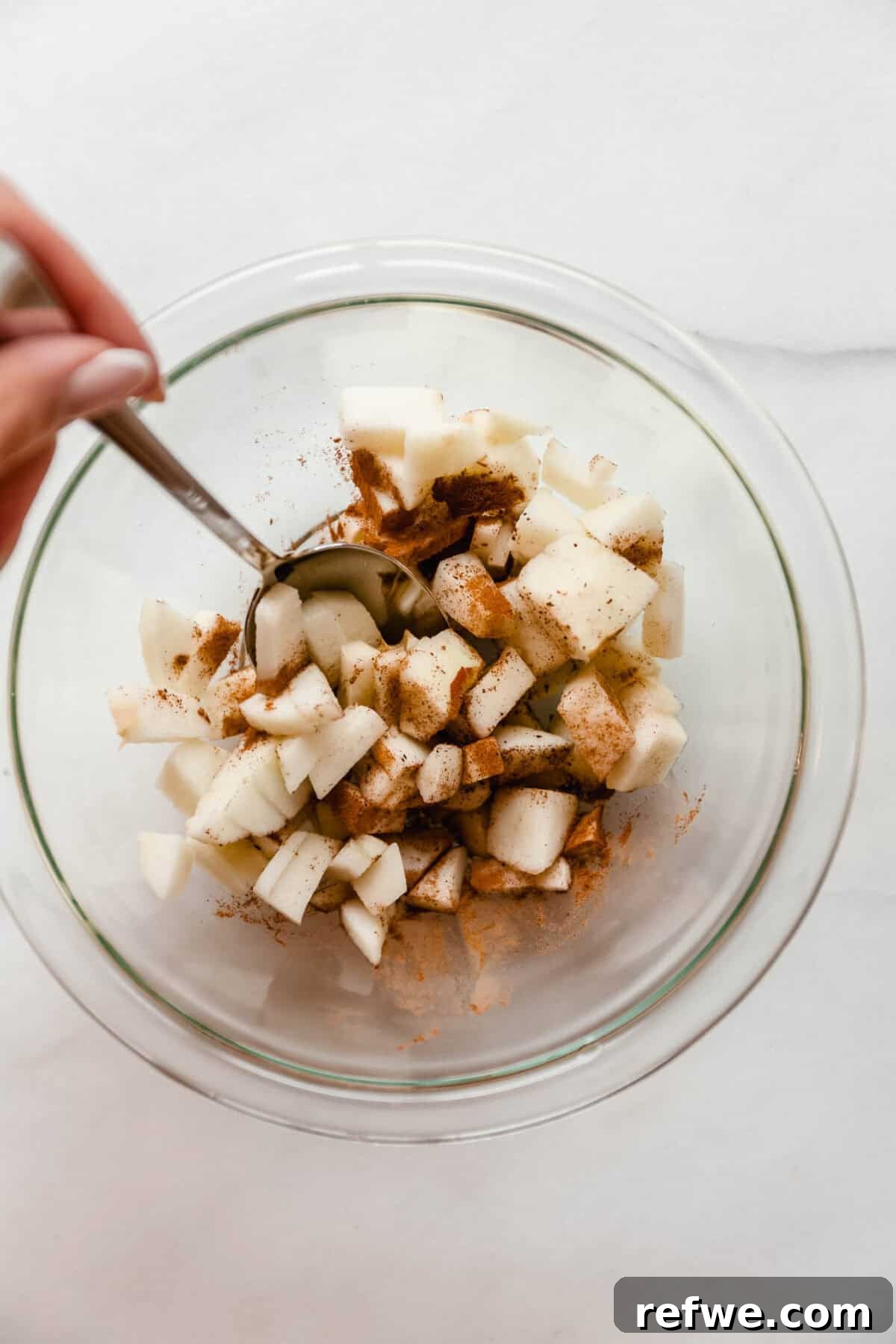 Air Fryer Apple Crisp Recipe — Quick Fall Dessert 4 Diced apples being tossed with cinnamon in a glass mixing bowl.