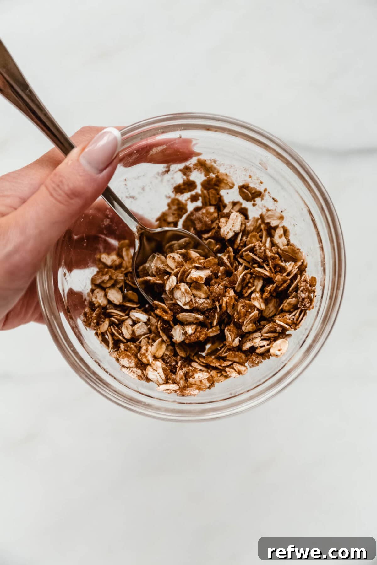 Air Fryer Apple Crisp Recipe — Quick Fall Dessert 5 A hand mixing the oat and cinnamon crisp topping in a glass bowl.