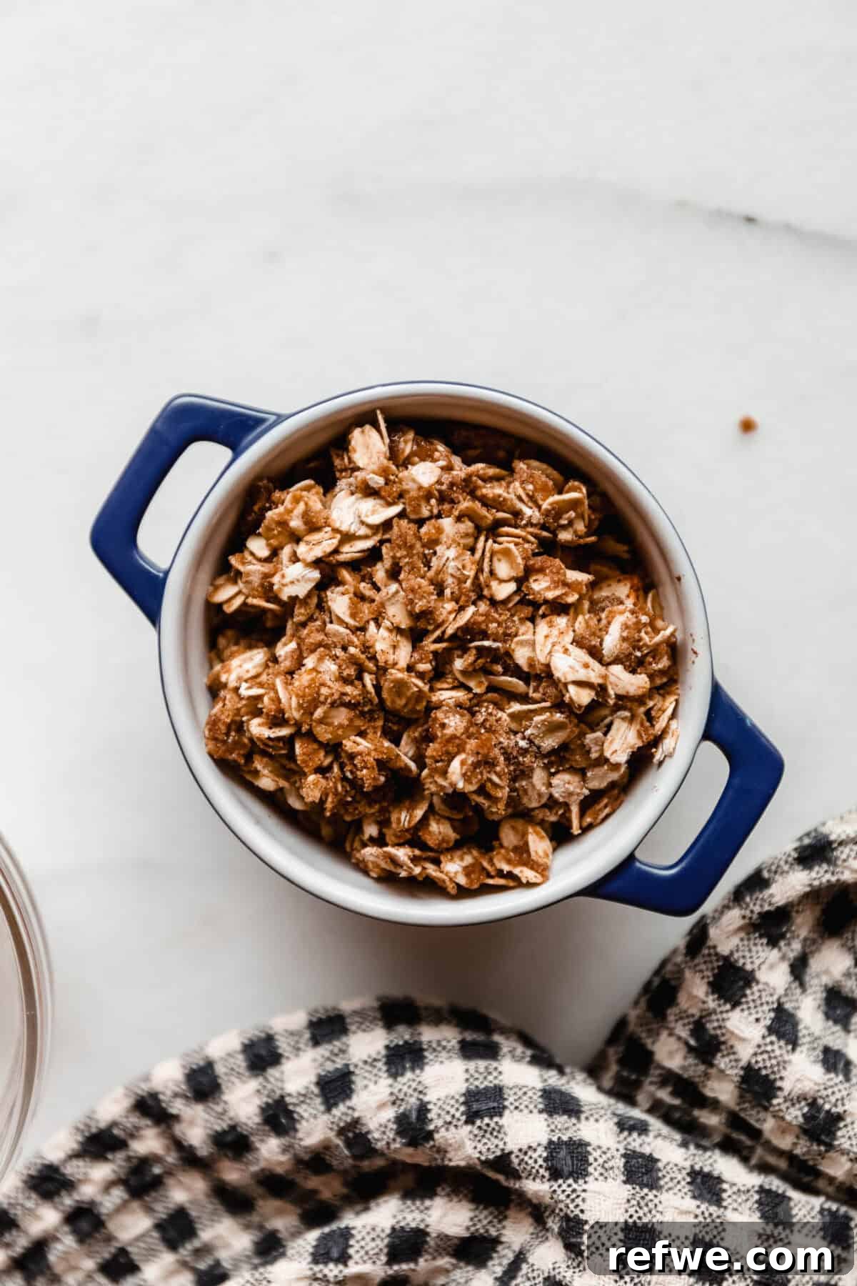 Air Fryer Apple Crisp Recipe — Quick Fall Dessert 6 An unbaked apple crisp topped with crumble mixture in a blue baking dish, ready for the air fryer.