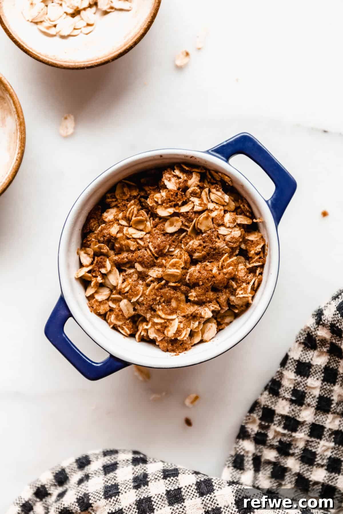 Air Fryer Apple Crisp Recipe — Quick Fall Dessert 7 Close-up of the assembled apple crisp with golden oat topping in a small blue dish before baking.