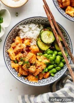 Overhead view of a bang bang chicken rice bowl garnished with sesame seeds and green onion.