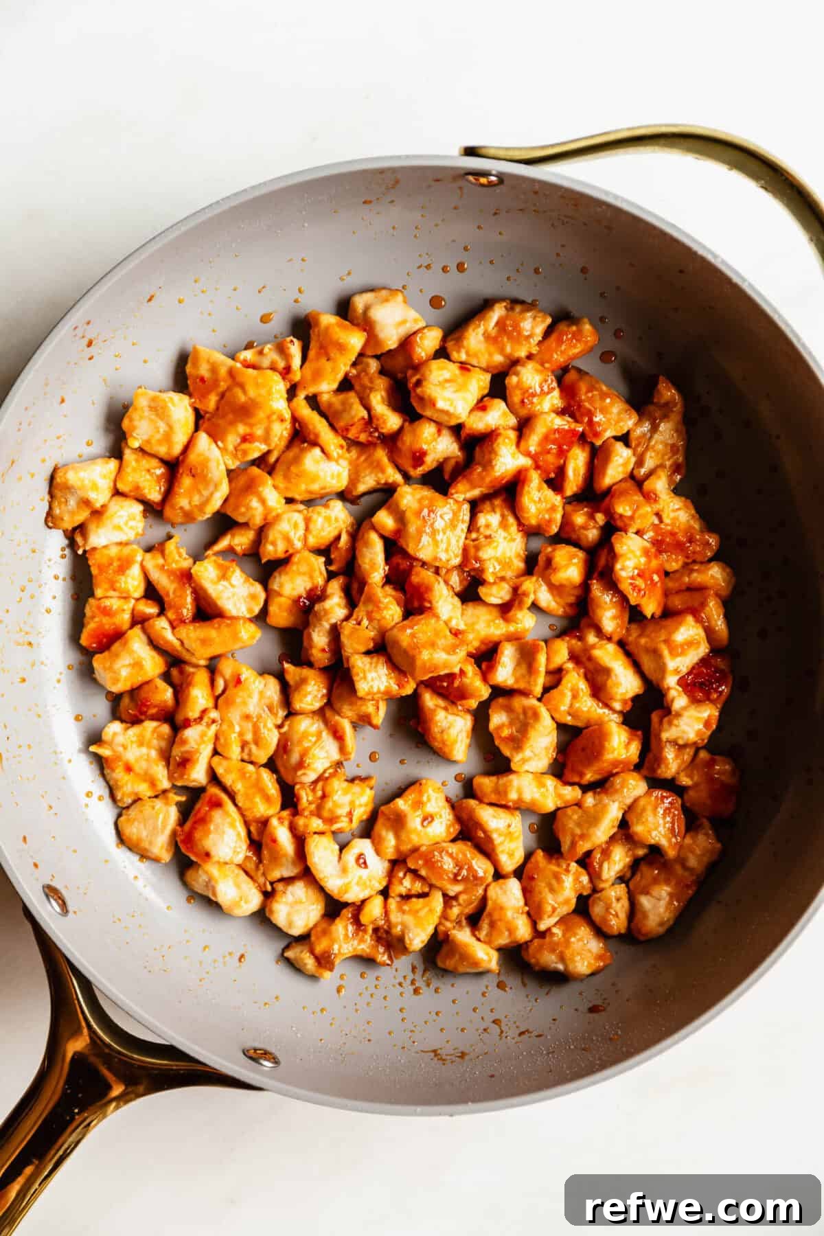 Bang Bang Chicken Bowl Recipe with Spicy Cucumber Salad 7 Golden brown chicken bites fully coated in bang bang sauce cooking in a skillet.