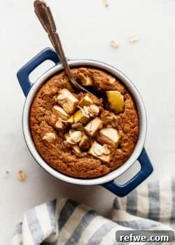 A single-serving apple baked oatmeal in a small blue dish topped with fresh apple slices and a spoon.