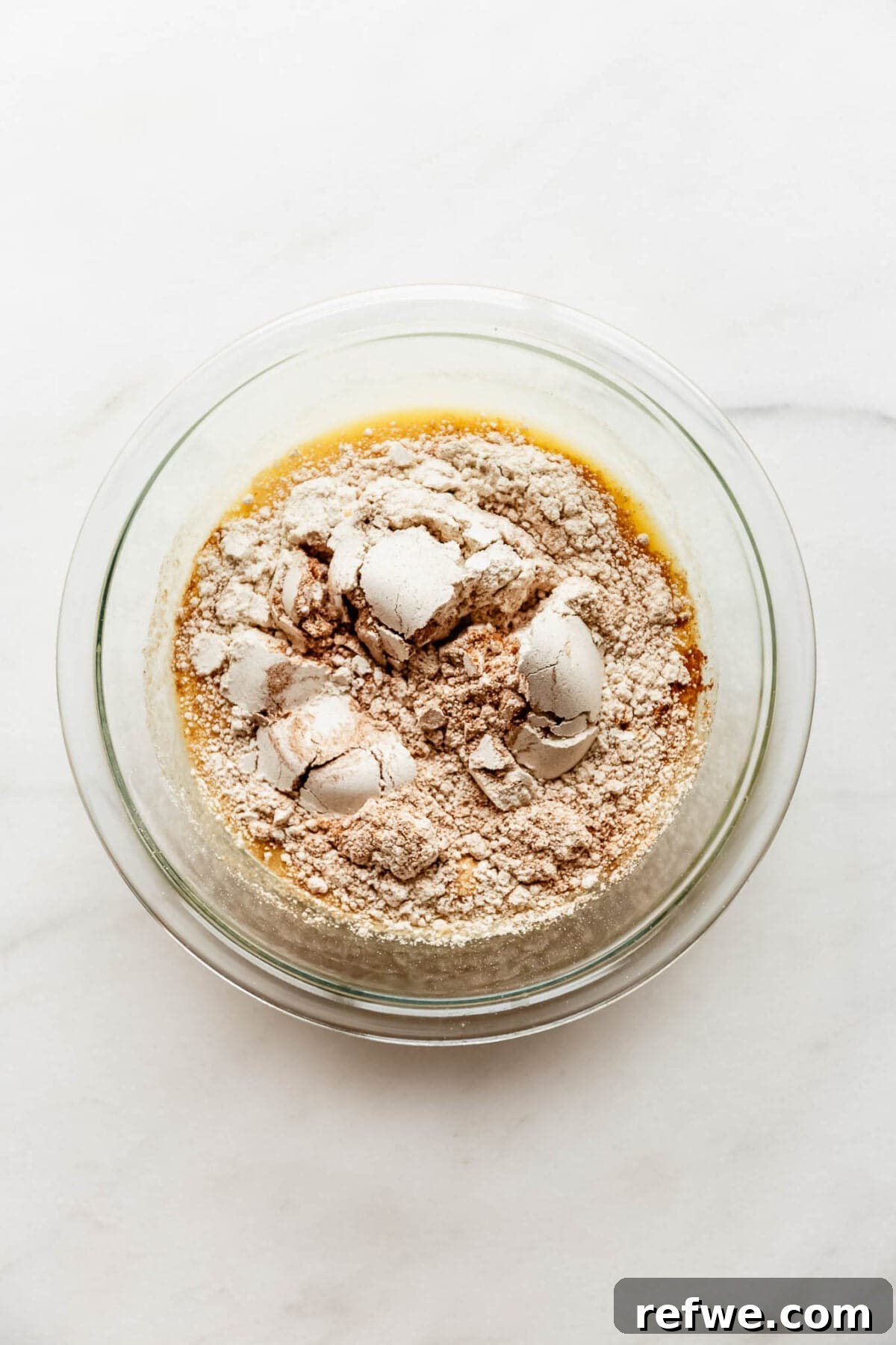 Apple Pie Baked Oats Recipe with Cinnamon 5 Dry flour and oat ingredients added on top of the wet mixture in a glass bowl before stirring.