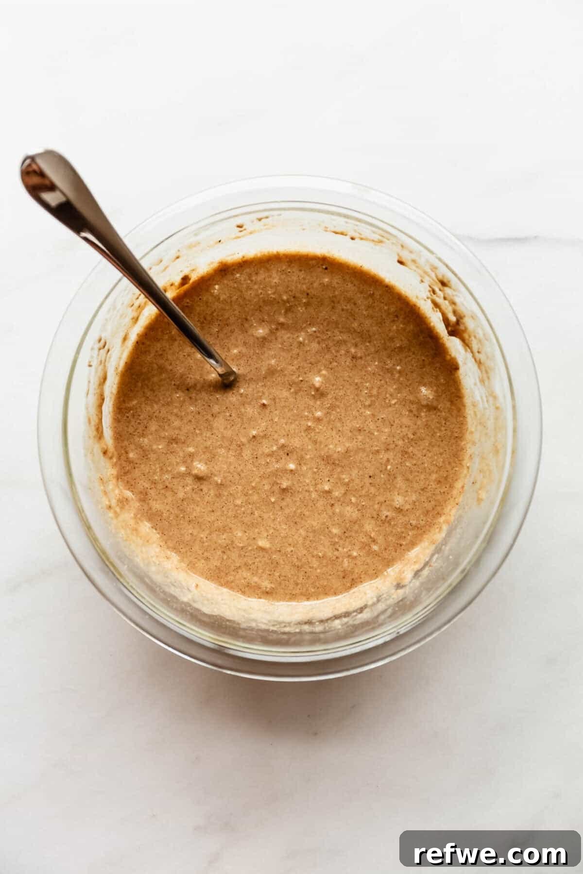 Apple Pie Baked Oats Recipe with Cinnamon 6 The combined oat batter in a glass jar with a spoon resting inside before portioning.