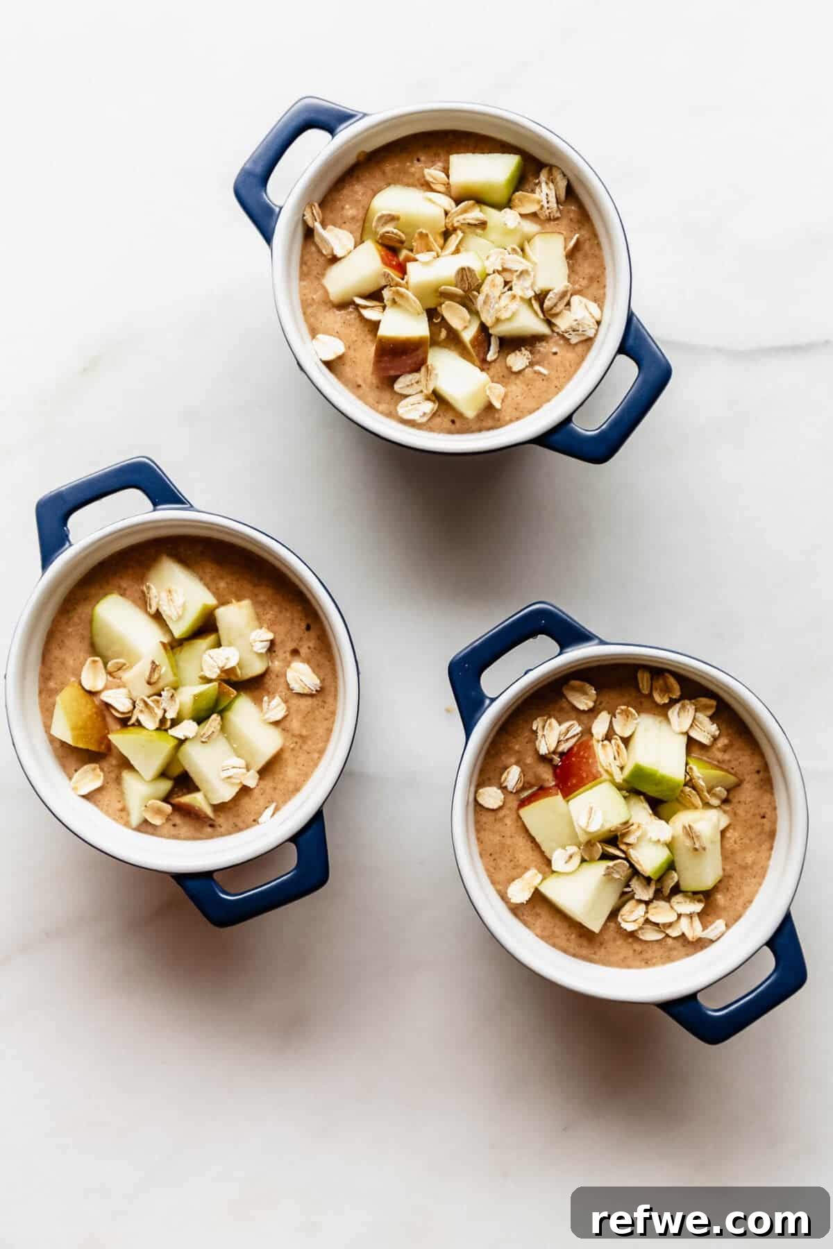 Apple Pie Baked Oats Recipe with Cinnamon 7 Overhead view of unbaked oat batter in three ramekins topped with diced apple and oats before baking.