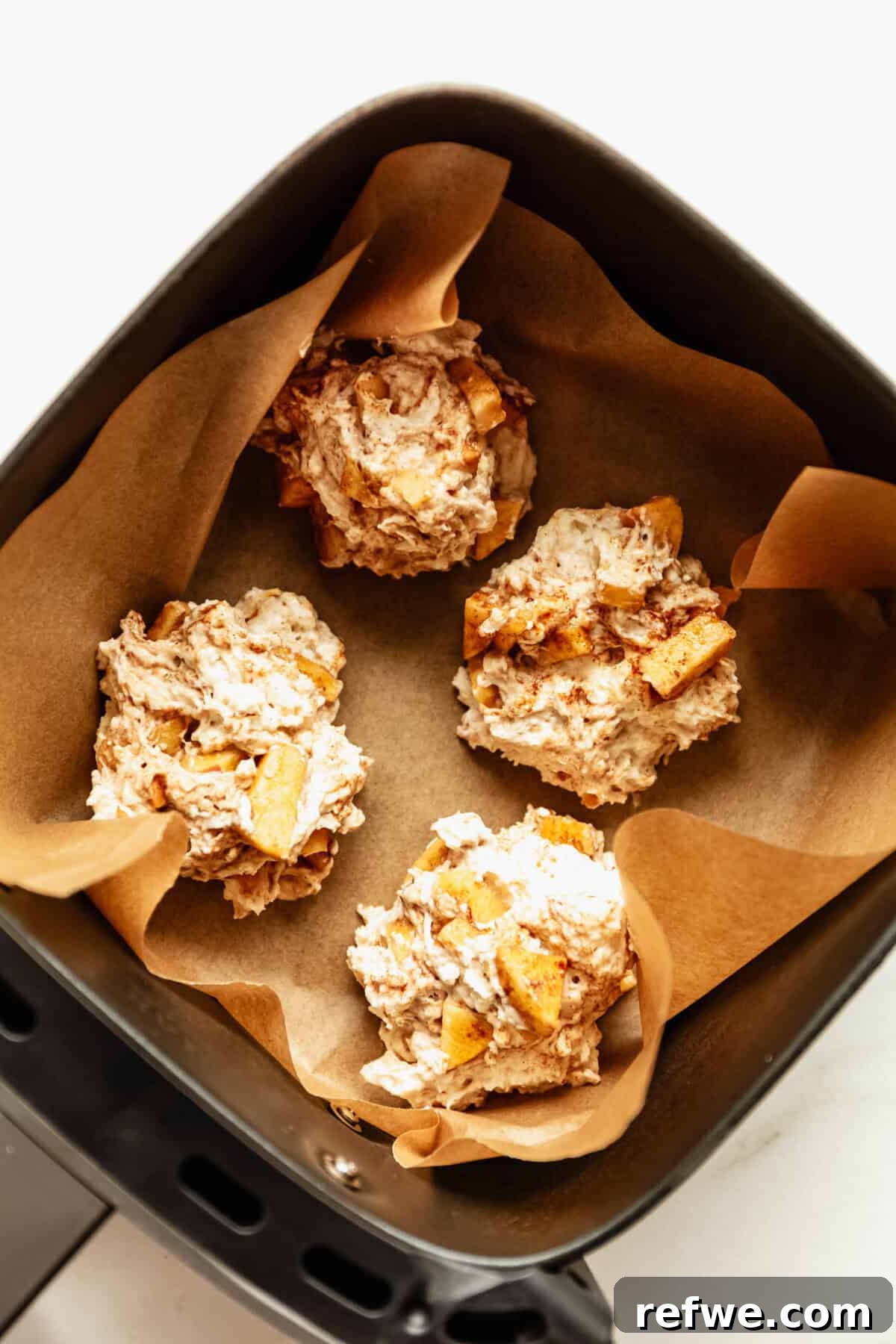 Cottage Cheese Apple Fritters with Maple Cinnamon Glaze 8 Scoops of cottage cheese apple fritter batter in an air fryer basket before cooking.