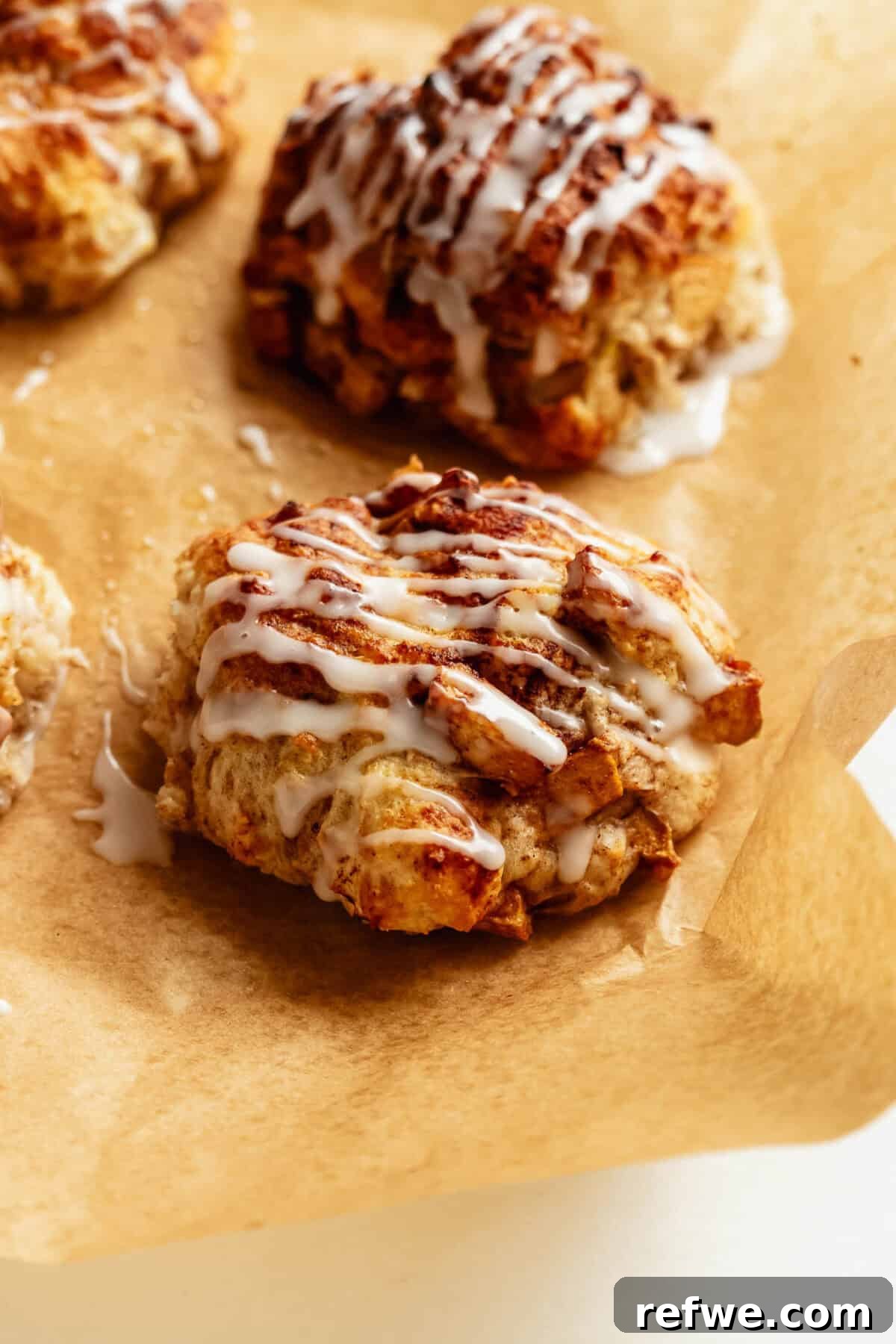Cottage Cheese Apple Fritters with Maple Cinnamon Glaze 10 Cottage cheese apple fritters drizzled with a sweet glaze on parchment paper.