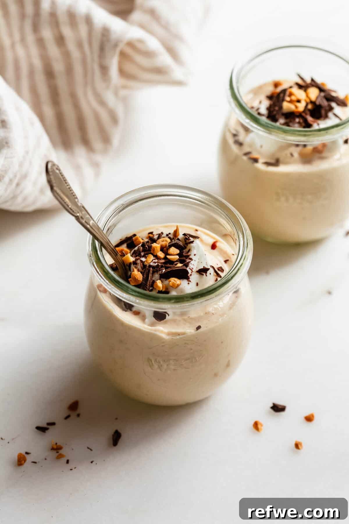 Creamy Greek Yogurt Peanut Butter Mousse Recipe 2 Two jars of Greek yogurt peanut butter mousse with a spoon, garnished with chopped nuts and chocolate.