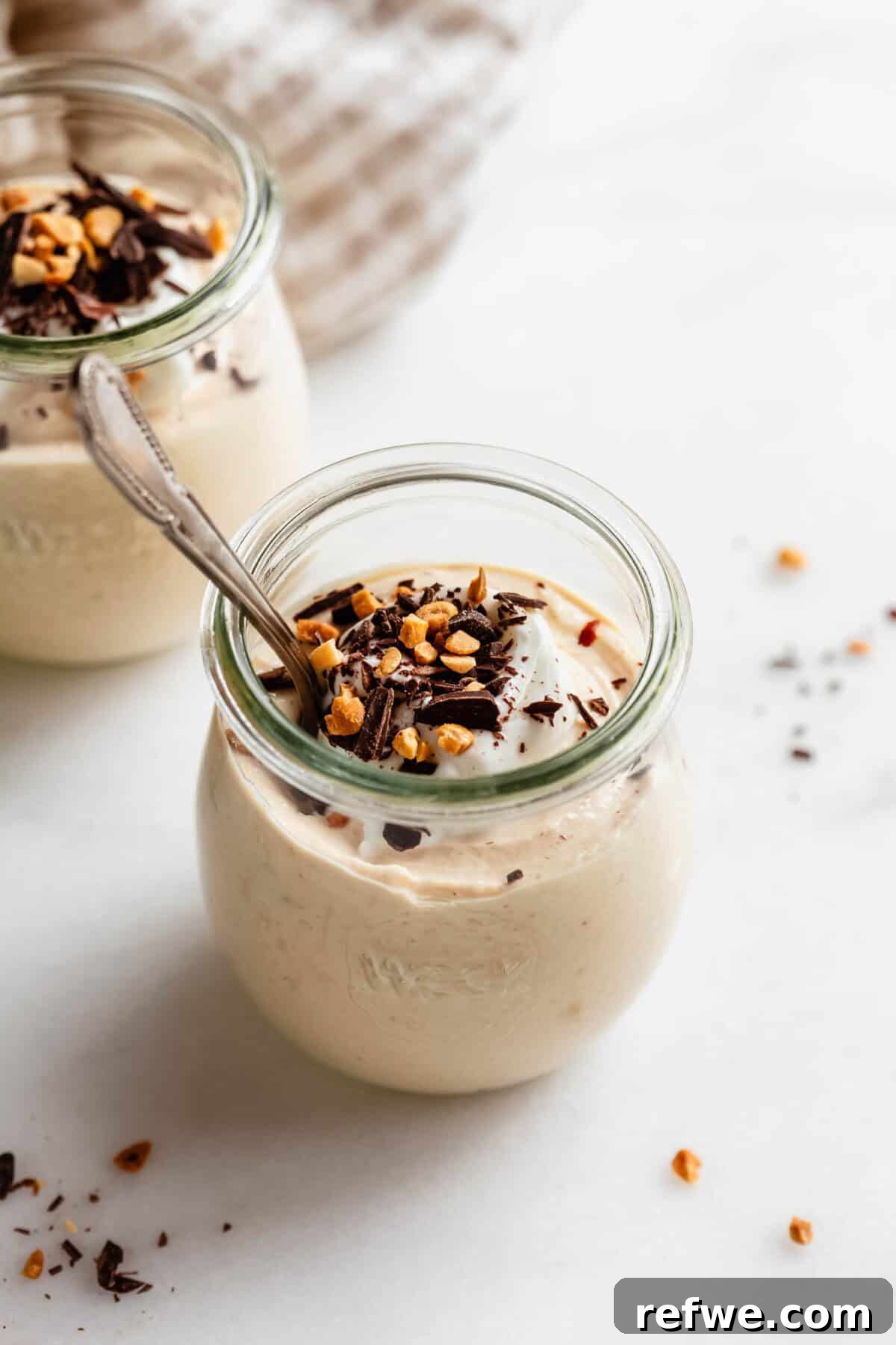 Creamy Greek Yogurt Peanut Butter Mousse Recipe 12 Jar of Greek yogurt peanut butter mousse with a spoon inside, topped with nuts and chocolate shavings.