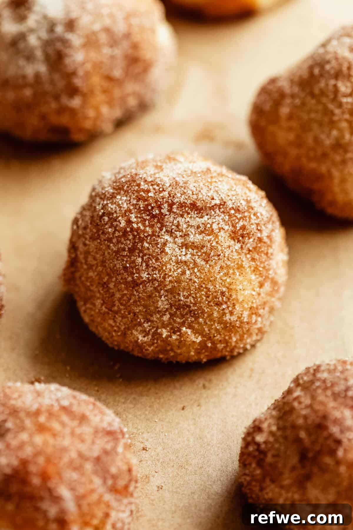 Baked Cottage Cheese Donut Holes Recipe 2 A close-up of golden donut holes coated in cinnamon sugar on parchment paper.