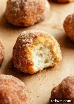 A cinnamon sugar donut hole torn open to reveal its soft, fluffy interior, surrounded by more donut holes.