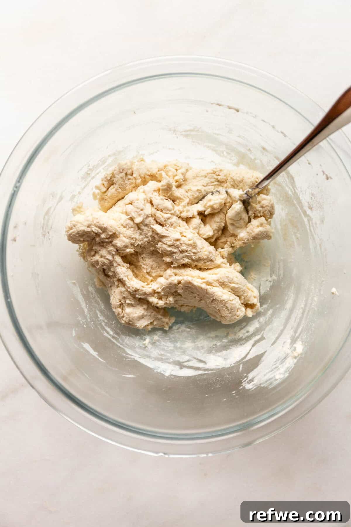 Baked Cottage Cheese Donut Holes Recipe 6 A glass bowl of thick, clumpy dough being mixed with a spoon.