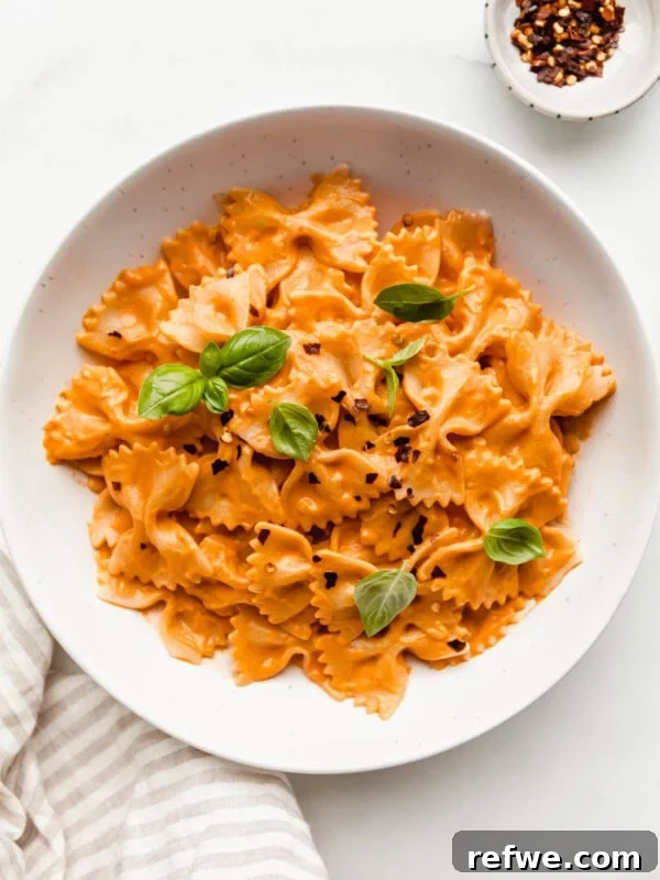 A bowl of vegan vodka pasta with a side of chili flakes and a napkin