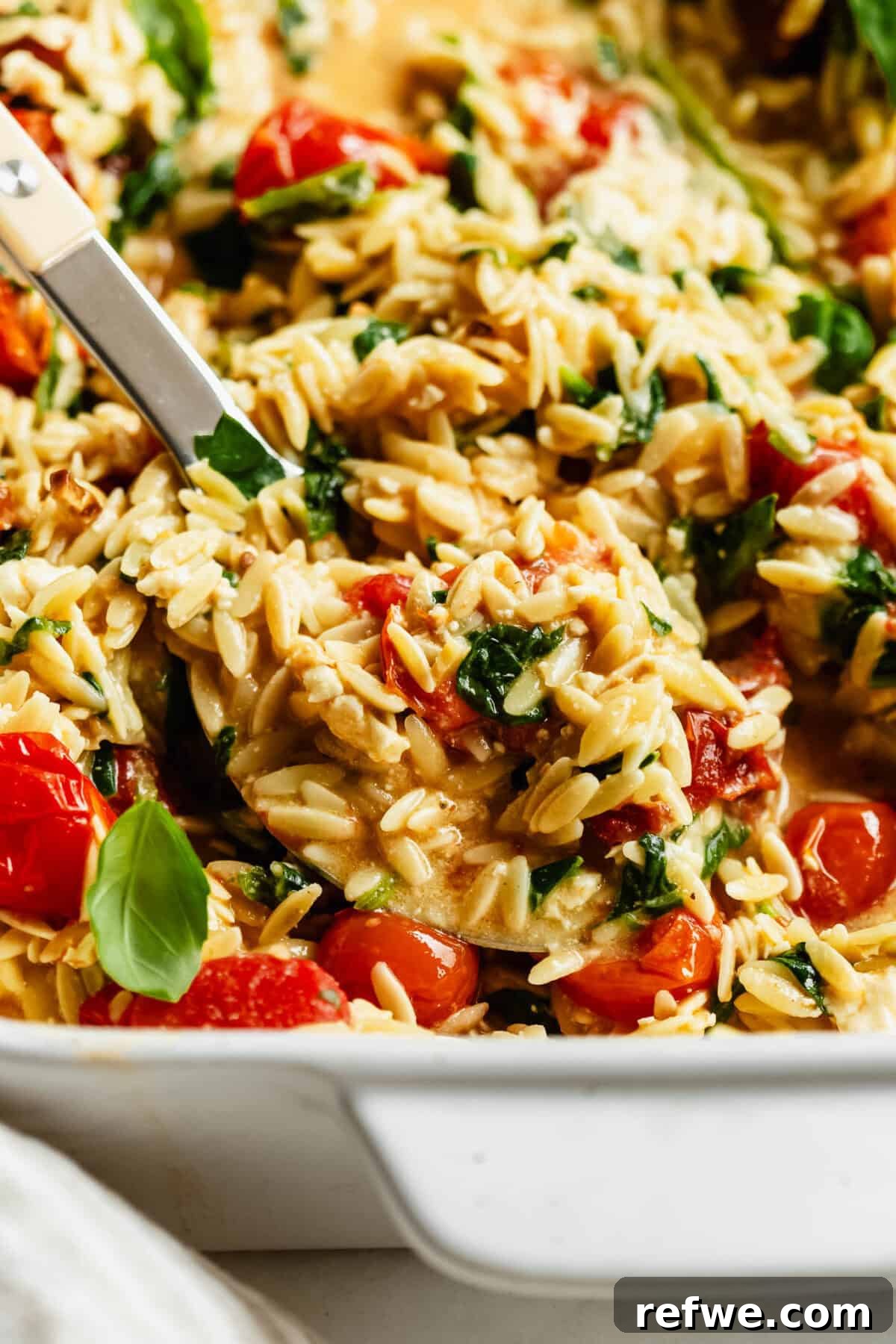 Creamy Baked Feta Orzo with Cherry Tomatoes and Spinach 13 Close-up of a spoon scooping baked feta tomato orzo from the dish.