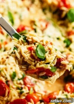 Fork lifting a bite of baked feta tomato orzo topped with fresh basil.