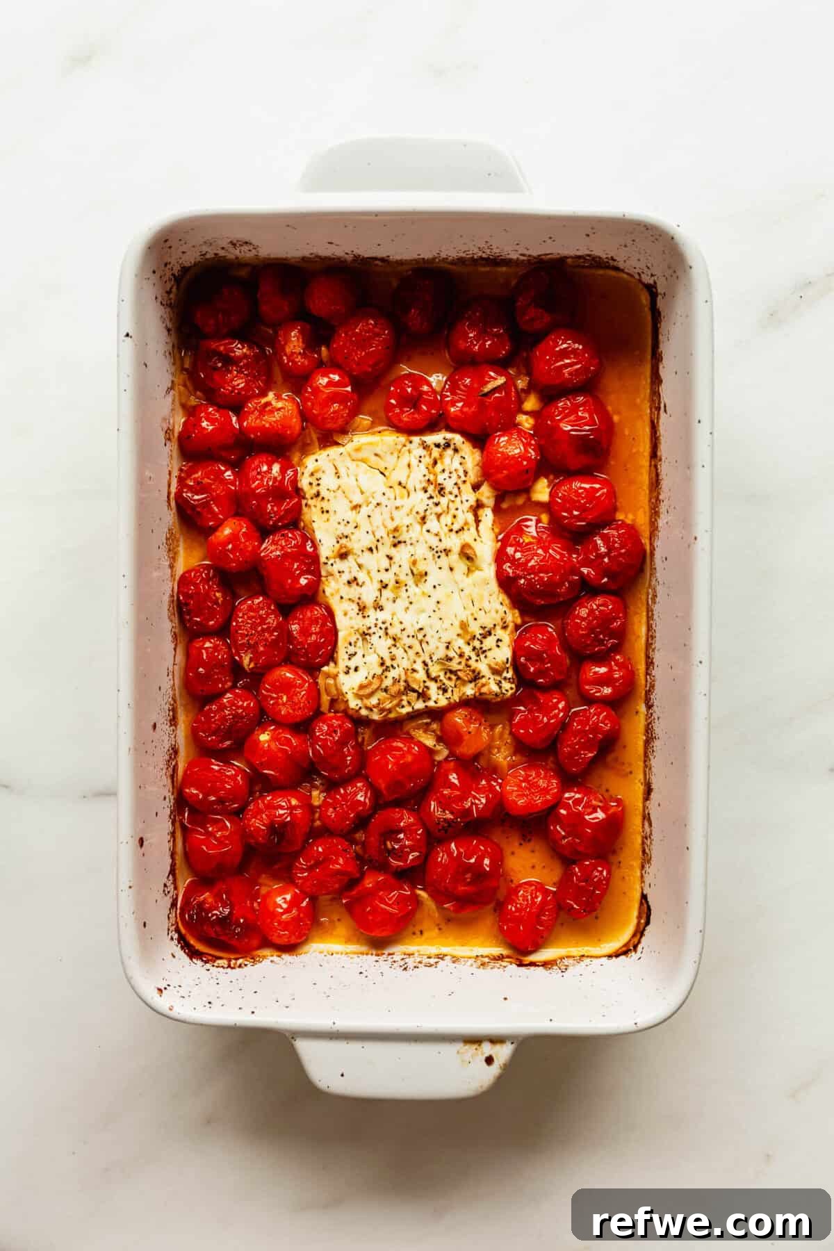 Creamy Baked Feta Orzo with Cherry Tomatoes and Spinach 5 Baking dish of roasted cherry tomatoes surrounding a block of feta cheese.