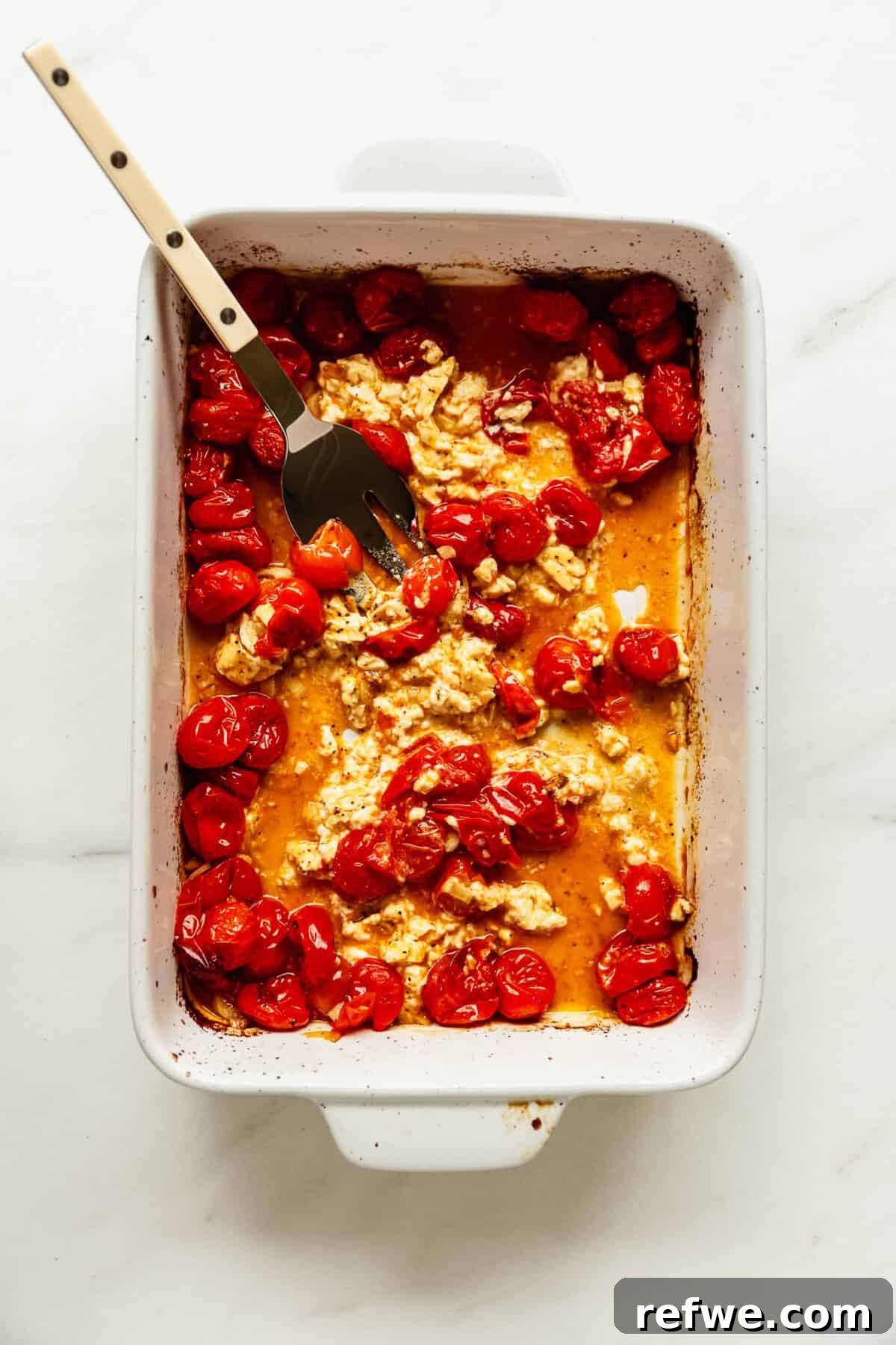 Creamy Baked Feta Orzo with Cherry Tomatoes and Spinach 6 Mashing baked feta cheese with roasted cherry tomatoes using a fork.