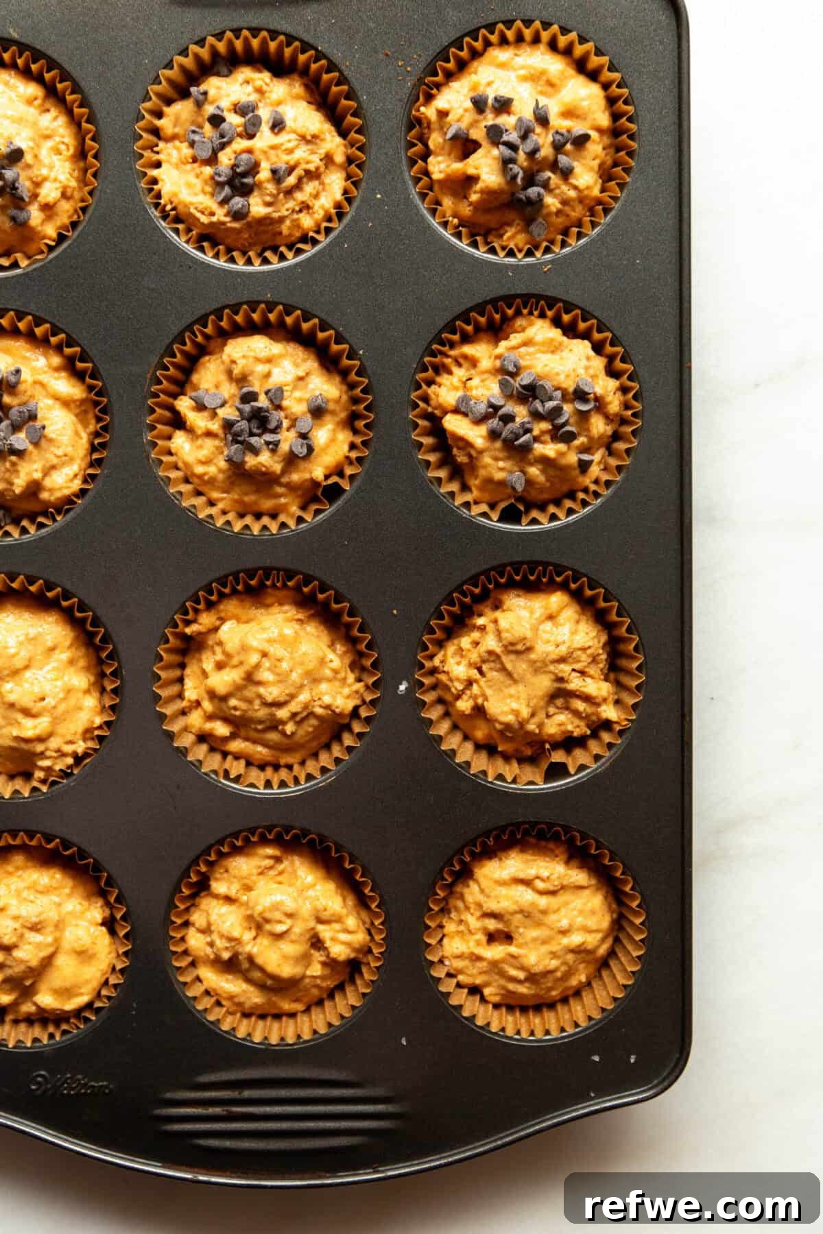 Moist Pumpkin Muffins with Cottage Cheese 8 Unbaked cottage cheese pumpkin muffin batter portioned into a muffin tin, some cups topped with chocolate chips.
